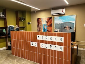 A reception area with a wooden partition displaying 'AIRBNB NO COPAN' and two framed artworks on the wall. - 2315B (São Paulo)
