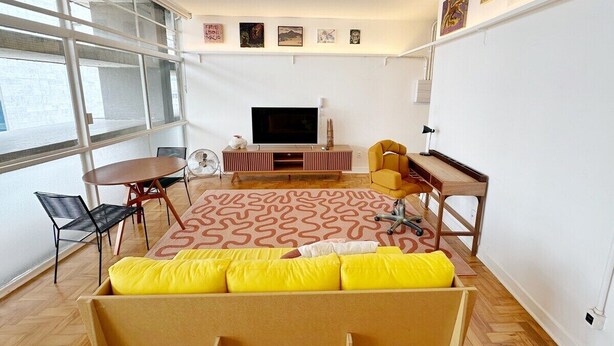 Un salon moderne doté d’une grande fenêtre, d’un téléviseur à écran plat, d’un canapé avec des coussins jaunes, d’une table basse et d’un tapis à motifs.