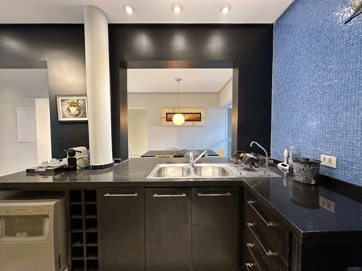 Una cocina moderna con pileta integrada, muebles oscuros y salpicadero de azulejos azules.