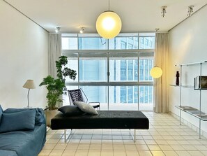 A modern living room with a black sofa, a black bench, a potted plant, and a large window with curtains. - 0121C (São Paulo)