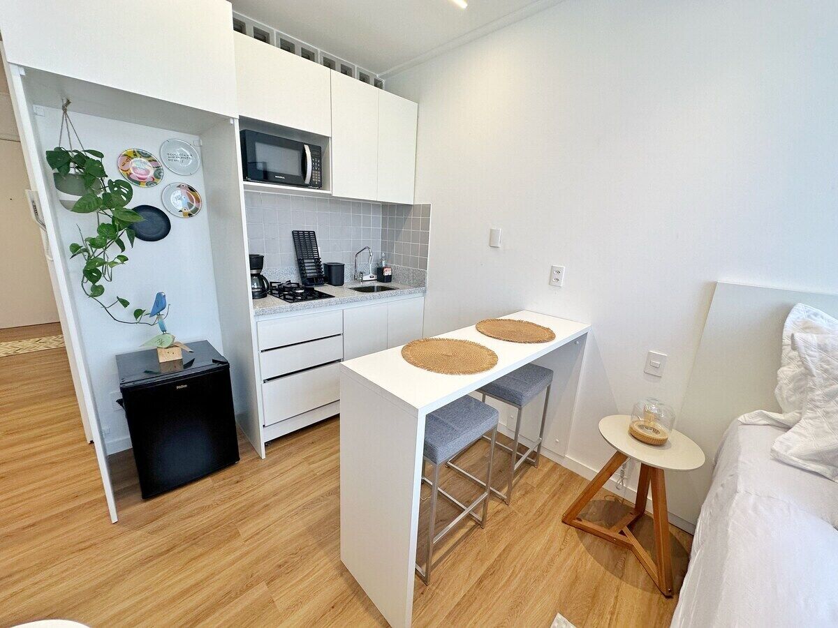 A compact kitchen with white cabinets, a microwave, and a small dining area with stools.