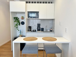 A compact kitchen with white cabinets, a microwave, a coffee maker, and two stools. - 1704B (São Paulo)