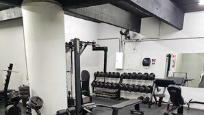 Un gimnasio con equipo de levantamiento de pesas, bancos y mancuernas.