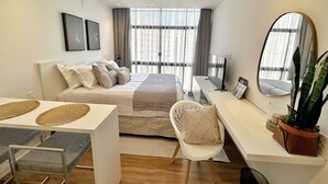 Un dormitorio moderno con cama, mesita de noche, silla, escritorio y un espejo grande.