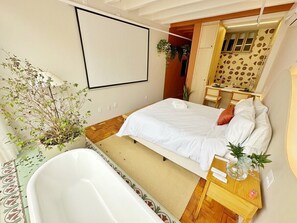 Ein Schlafzimmer mit Bett, Nachttisch, Spiegel, Fenster und einem Badezimmer mit Badewanne.
