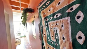 Ein Flur mit Teppichmuster, einer hängenden Pflanze und Blick in einen Raum mit Bett und Fenster.