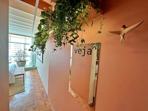 A hallway with a wooden floor, a potted plant, a mirror with the word 'veja' on it, and a wooden bird sculpture.