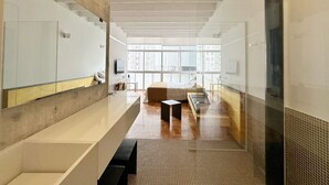 A modern hotel room with a large window, a bed, a small table, and a seating area. - 0713B (São Paulo)