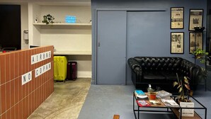 A hotel lobby with a reception desk, a black leather couch, a coffee table with magazines, and a door to a room. - 0713B (São Paulo)