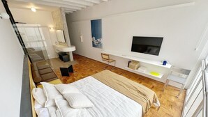 A modern bedroom with a large bed, a TV mounted on the wall, and a small desk area. - 0713B (São Paulo)