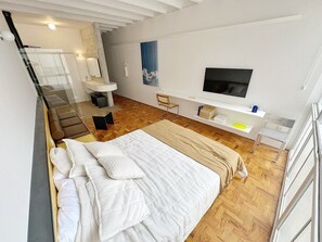 A modern bedroom with a large bed, a TV mounted on the wall, and a small desk area. - 0713B (São Paulo)