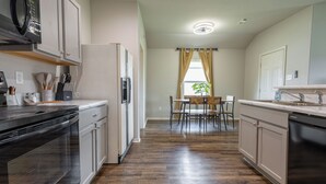 Une cuisine moderne équipée d’un four à micro-ondes, d’un réfrigérateur et d’un lave-vaisselle. On y trouve également un coin repas avec une table et des chaises, ainsi qu’une fenêtre avec des rideaux.