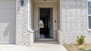 Une maison avec une façade en briques, un portail de garage et un petit jardin devant, agrémenté d’une plante.