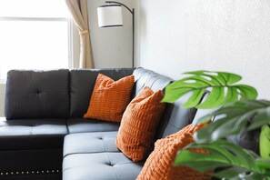 Een moderne woonkamer met een donker leren bank, oranje kussens en een groene plant.