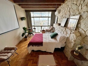 A bedroom with a large bed, a stone wall, a view of the city, and a wooden floor. - 2911B (São Paulo)