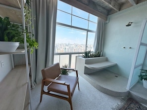 Ein modernes Zimmer mit großem Fenster, einem Holzstuhl, einer eingebauten Sitzbank und einer kleinen Pflanze.