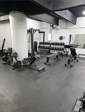 Un gimnasio con equipo de levantamiento de pesas, bancos y mancuernas.