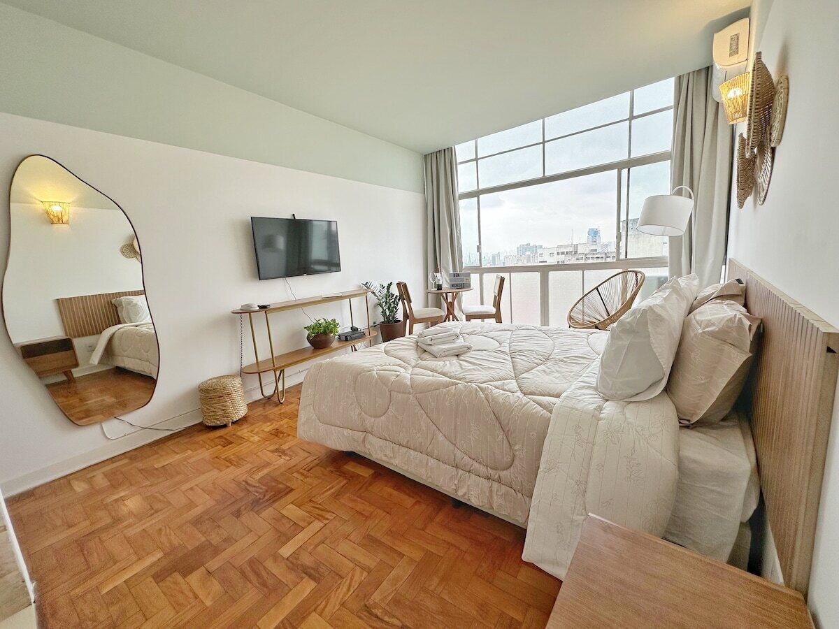 Une chambre moderne avec un grand lit, une télévision, une fenêtre donnant sur un beau paysage et un miroir.