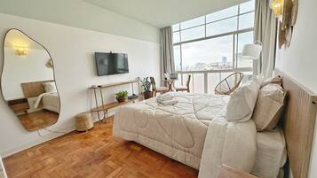 Une chambre moderne avec un grand lit, une télévision, une fenêtre donnant sur un beau paysage et un miroir.