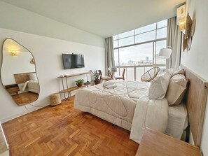 A modern bedroom with a large bed, a television, a window with a view, and a mirror. - 2407B (São Paulo)