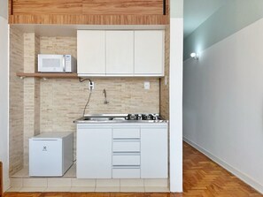Una cocina compacta con microondas, refrigerador pequeño y estufa a gas.