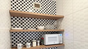Eine Küche mit Mikrowelle, Kaffeemaschine und Tassen auf Regalen.