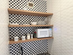 A kitchen with a microwave, coffee maker, and mugs on shelves. - 2406B (São Paulo)
