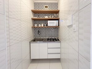 A compact kitchen with white cabinets, a microwave, a gas stove, and a sink. - 2406B (São Paulo)