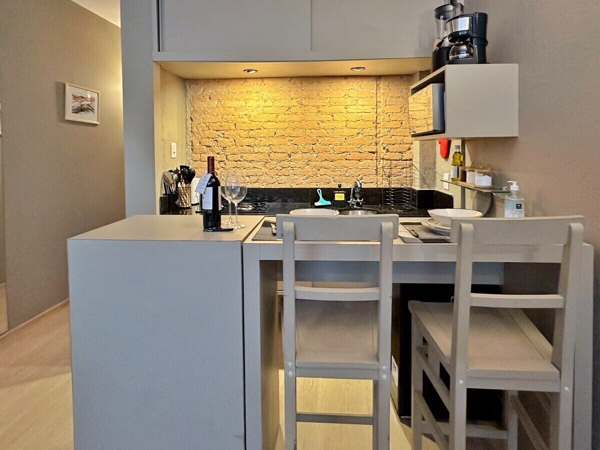 A compact kitchen with a stone backsplash, a coffee machine, and a wine bottle on the counter.