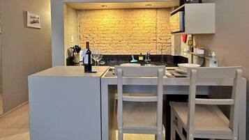 A compact kitchen with a stone backsplash, a coffee machine, and a wine bottle on the counter.