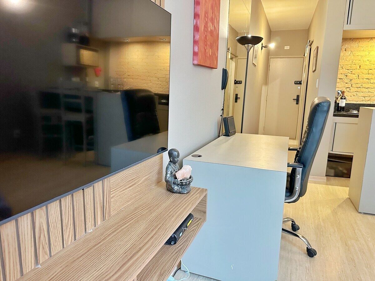 A modern office space with a wooden desk, a chair, a small statue, and a kitchen area in the background.