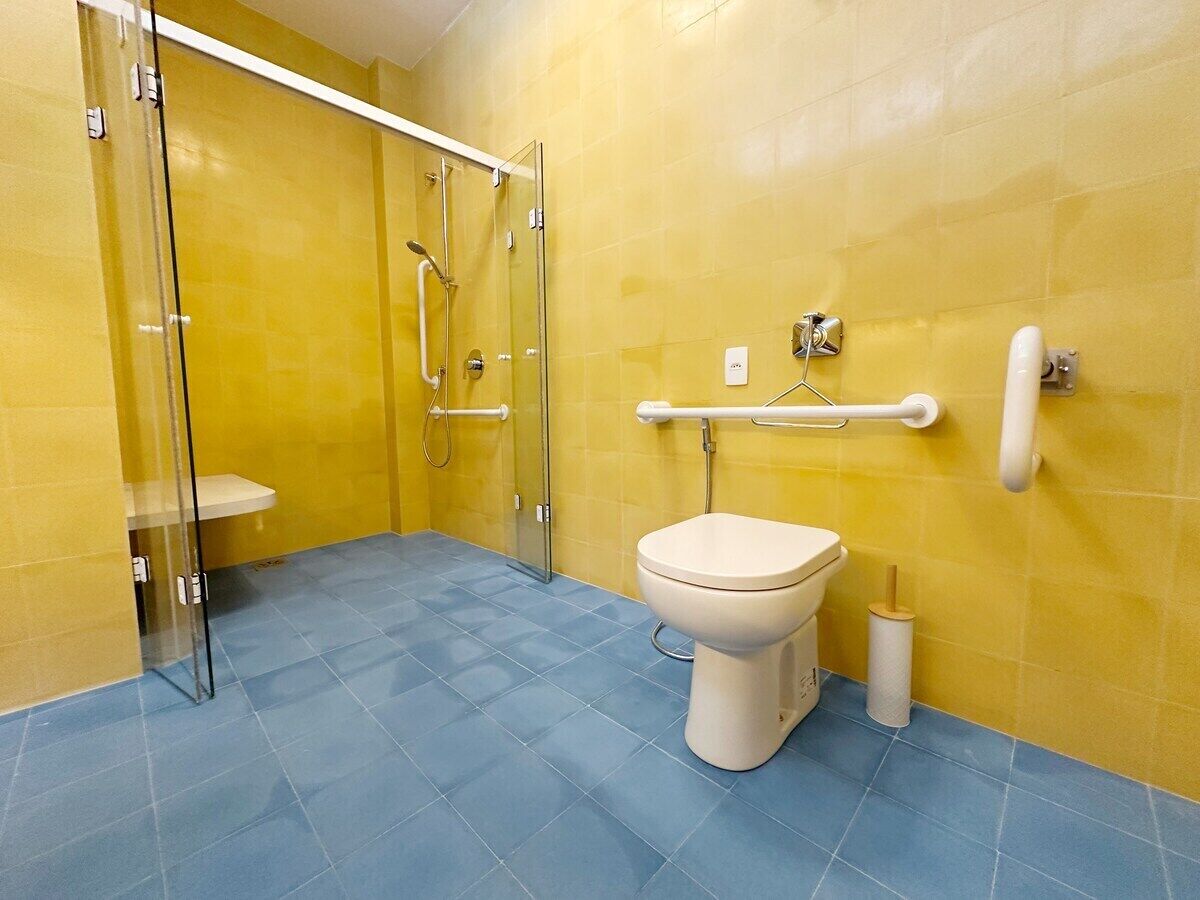 A bathroom with a glass shower enclosure, a toilet, and a handrail.