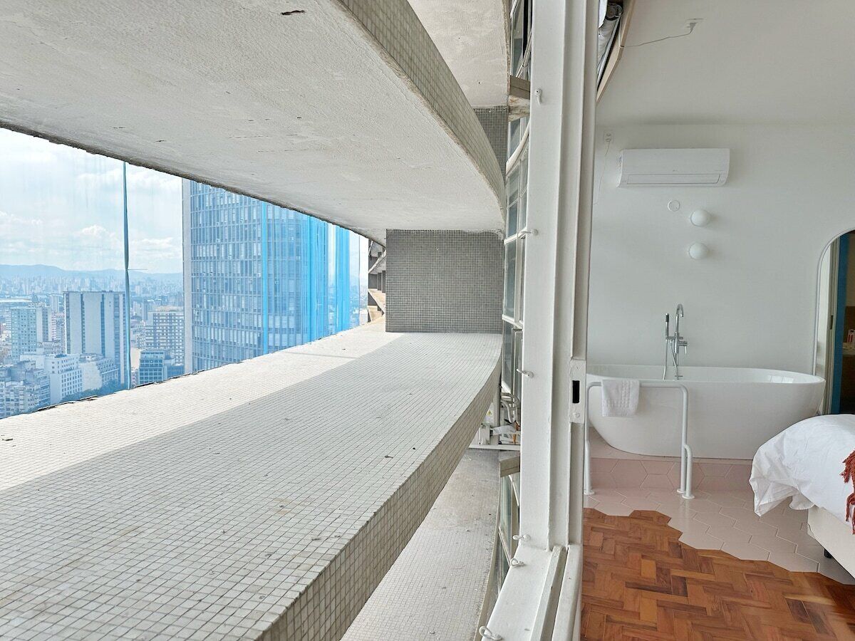 A high-rise hotel room with a city view, a bathtub, and a balcony.