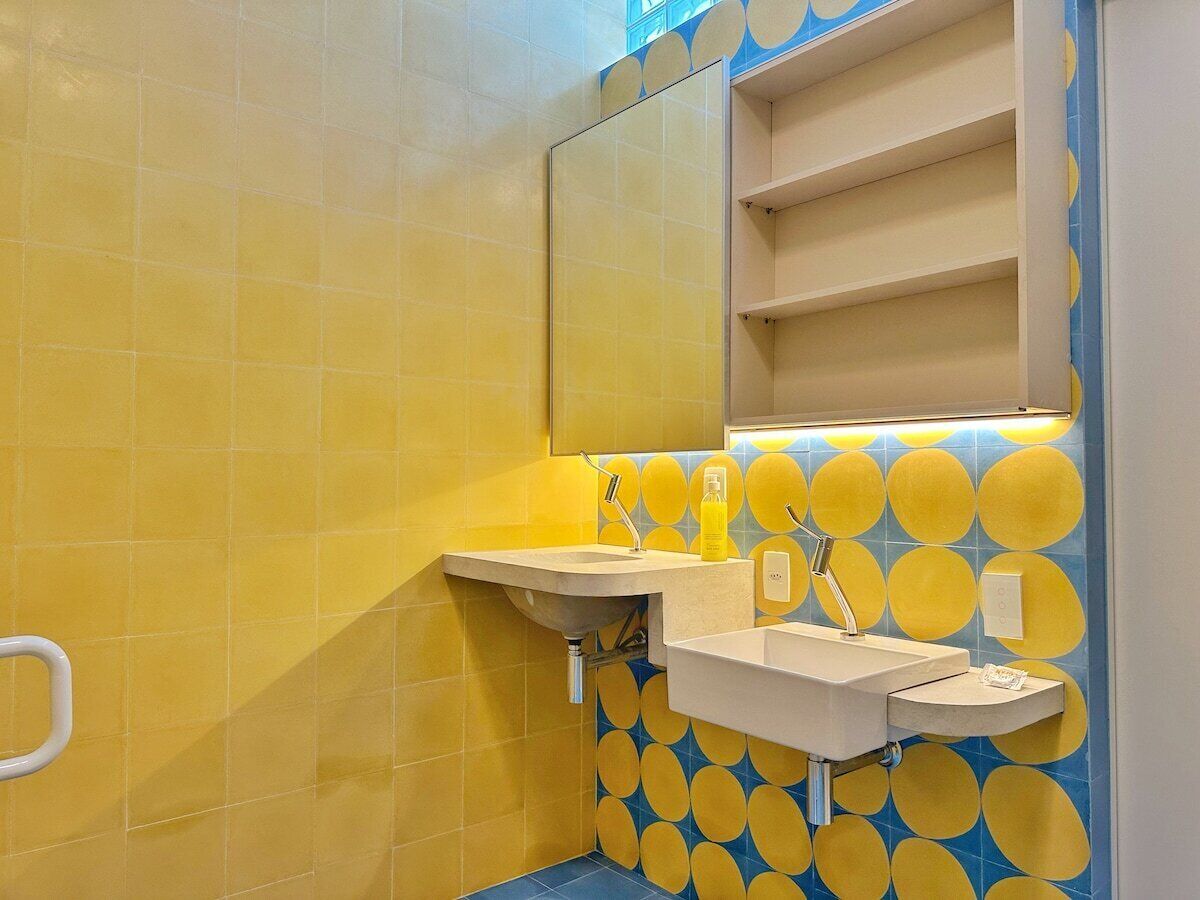 A bathroom with yellow tiles, a sink, a mirror, and a shelf.