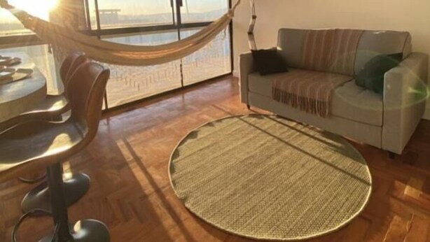 A room with a hammock, a round woven rug, a sofa, and a wall with a cityscape painting.