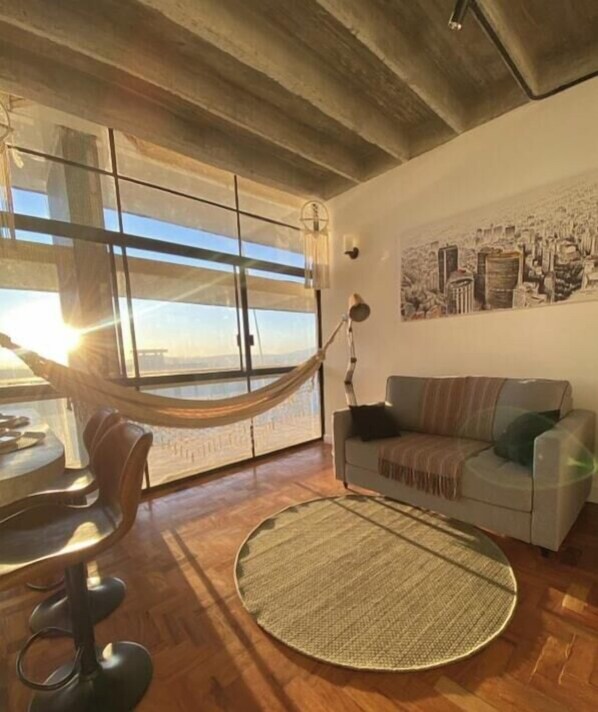 A room with a hammock, a round woven rug, a sofa, and a wall with a cityscape painting.