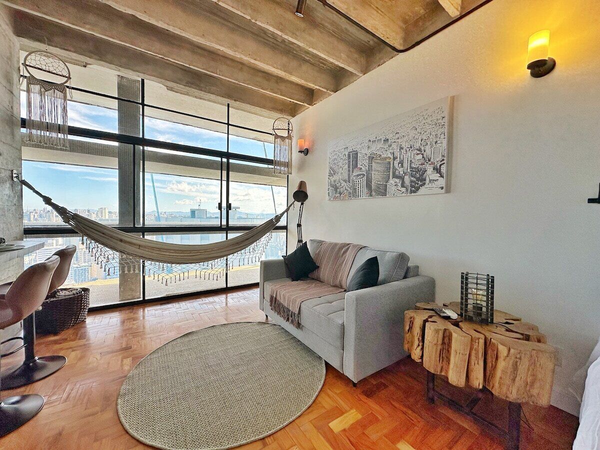 A modern living room with a hammock, a grey sofa, a round rug, and a wooden side table.