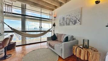 A modern living room with a hammock, a grey sofa, a round rug, and a wooden side table.