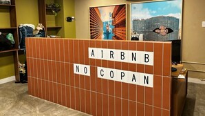 A reception area with a wooden partition displaying 'AIRBNB NO COPAN' and two framed pictures on the wall.
