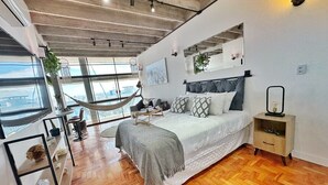 A modern bedroom with a large bed, a nightstand, a hammock, and a view of the outdoors.