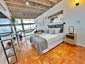 A modern bedroom with a large bed, a nightstand, a hammock, and a view of the outdoors.