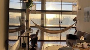 A modern living room with a hammock, large windows, and a view of the city.