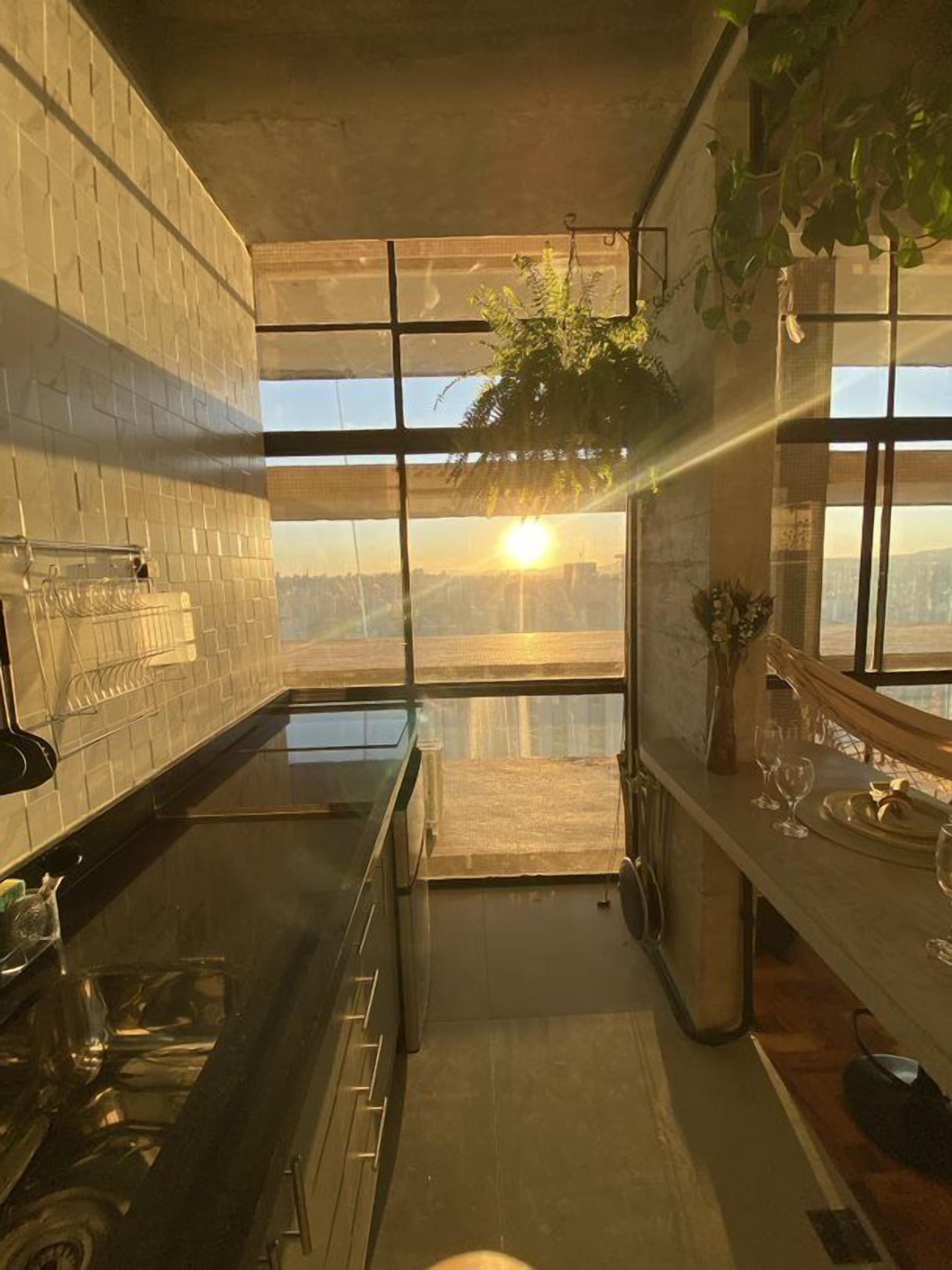 A kitchen with a large window, a black countertop, and hanging plants.