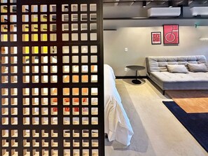 A room with a bed, a sofa, a wall with a framed picture, and a decorative partition with square cutouts. - 0141F (São Paulo)