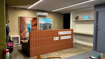 Un espace d’accueil avec un panneau de séparation marron sur lequel est inscrit « AIRBNB NO COPAN » et une peinture représentant un paysage urbain.
