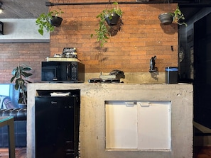 A kitchen area with a brick wall, a microwave, a small refrigerator, and hanging plants. - 3013M (São Paulo)
