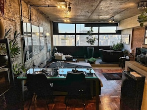 A dining area with a table set for two, a city view through large windows, and a modern kitchen in the background. - 3013M (São Paulo)