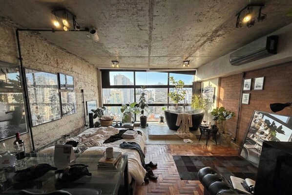 A modern hotel room with a large bed, a glass table, a city view, and a brick wall. - 3013M (São Paulo)