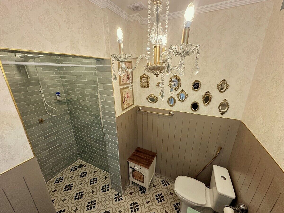 Een badkamer met douche, toilet, wastafel en een kroonluchter.