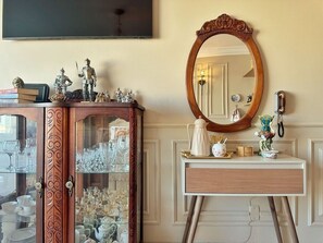 A room with a wooden cabinet displaying glassware, a white console table with a mirror and decorative items, and a wall-mounted telephone. - 2312B (São Paulo)